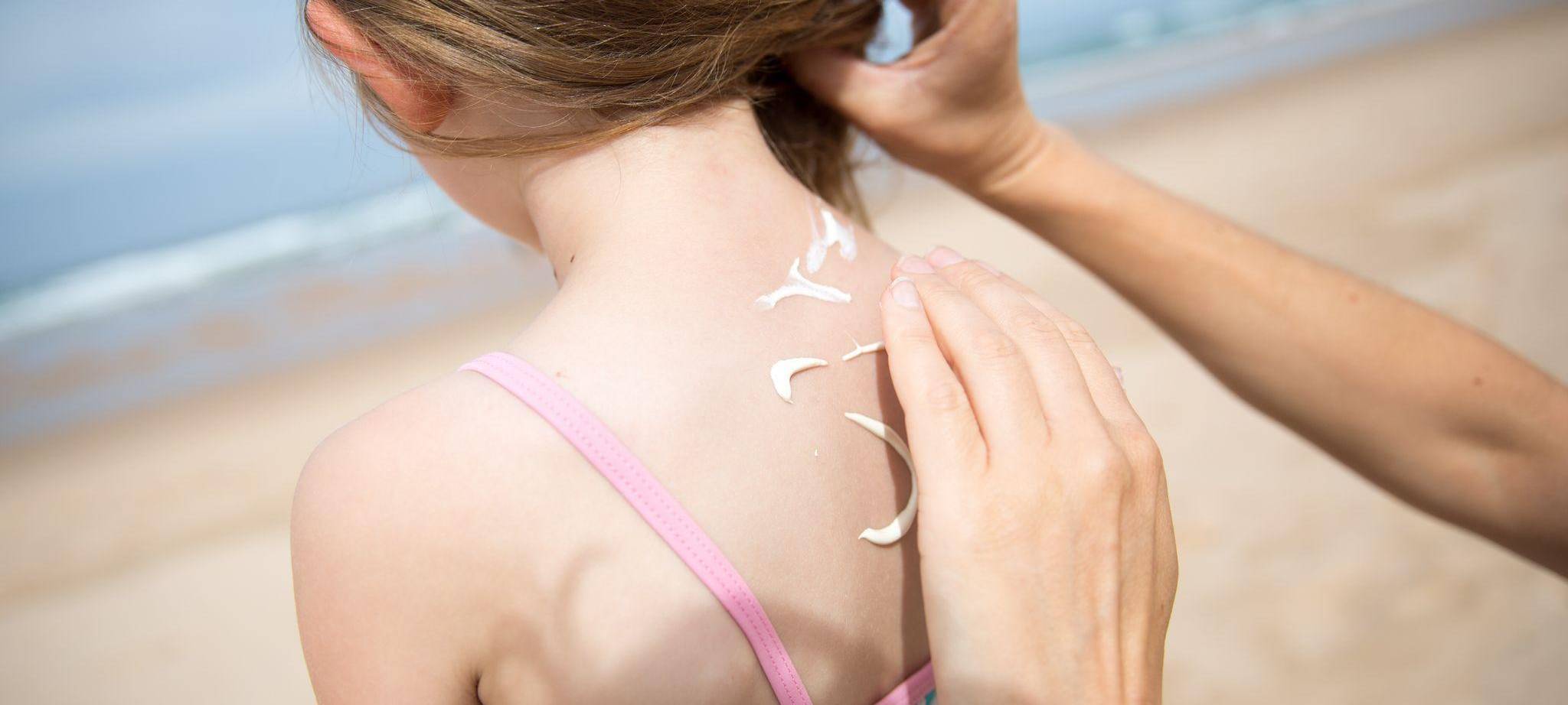 Eine Frau cremt ihre Tochter mit Sonnencreme ein