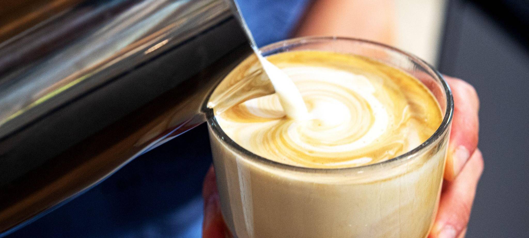 Milch wird in einen Kaffee gegossen