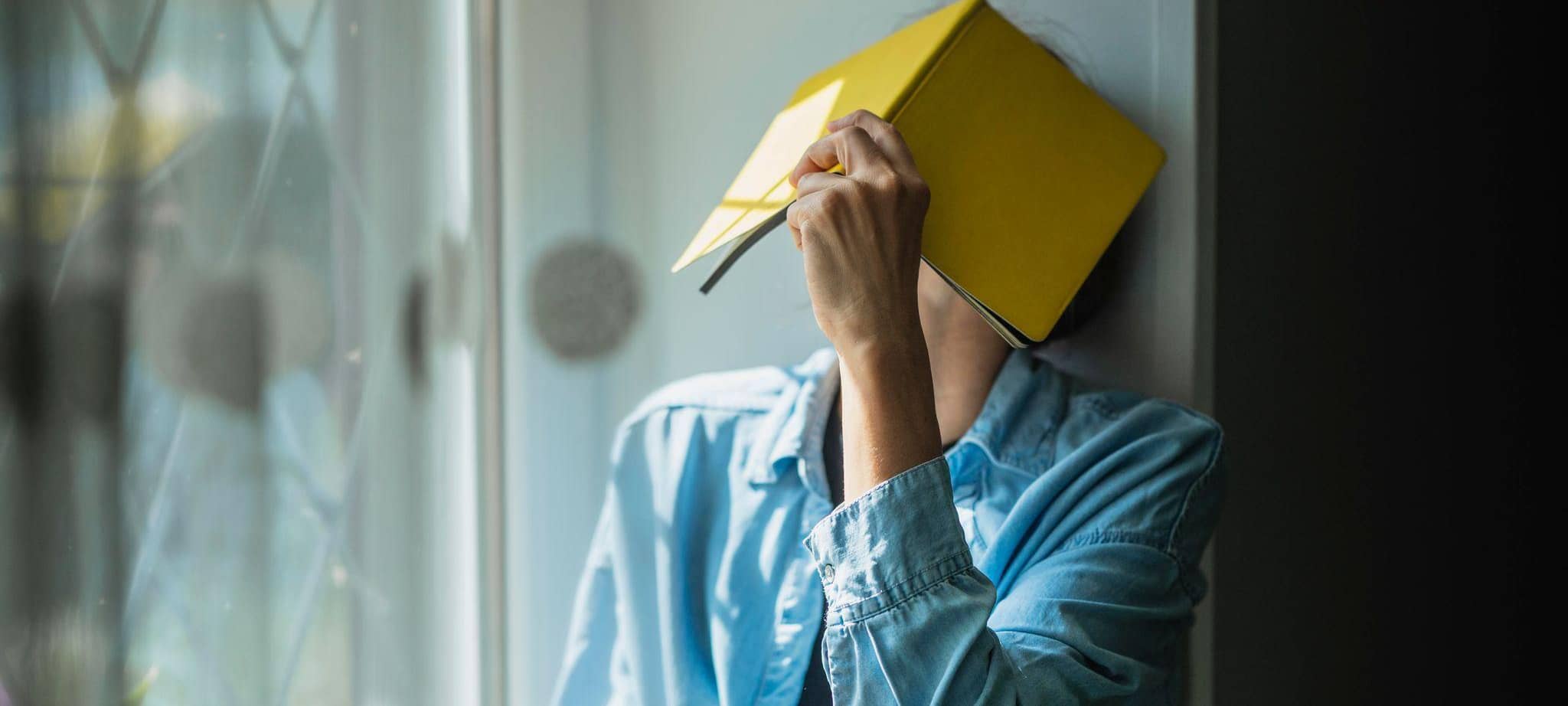 Frau versteckt ihr Gesicht hinter einem Buch